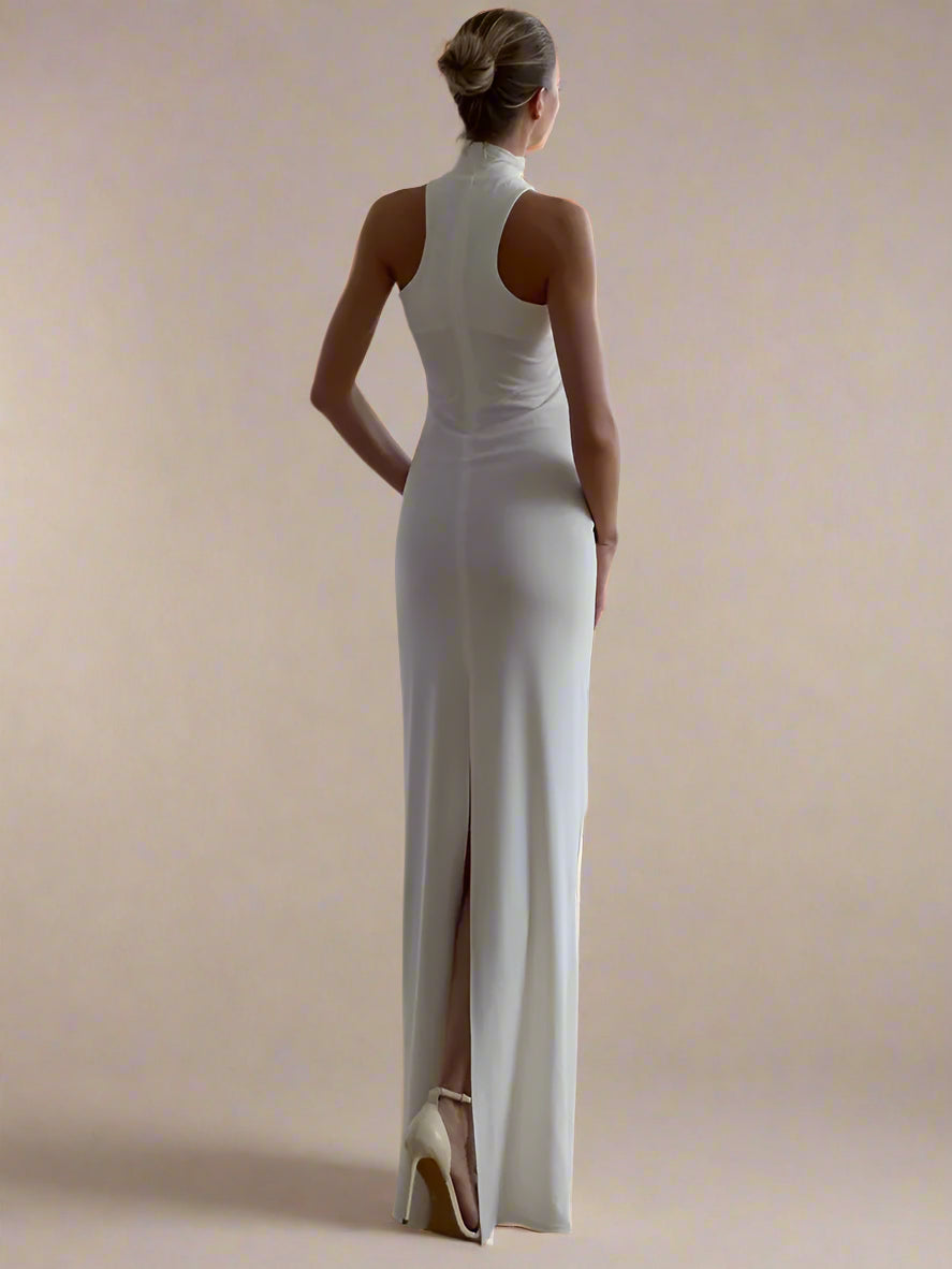 Woman in a white evening gown standing in a room with light-colored curtains.